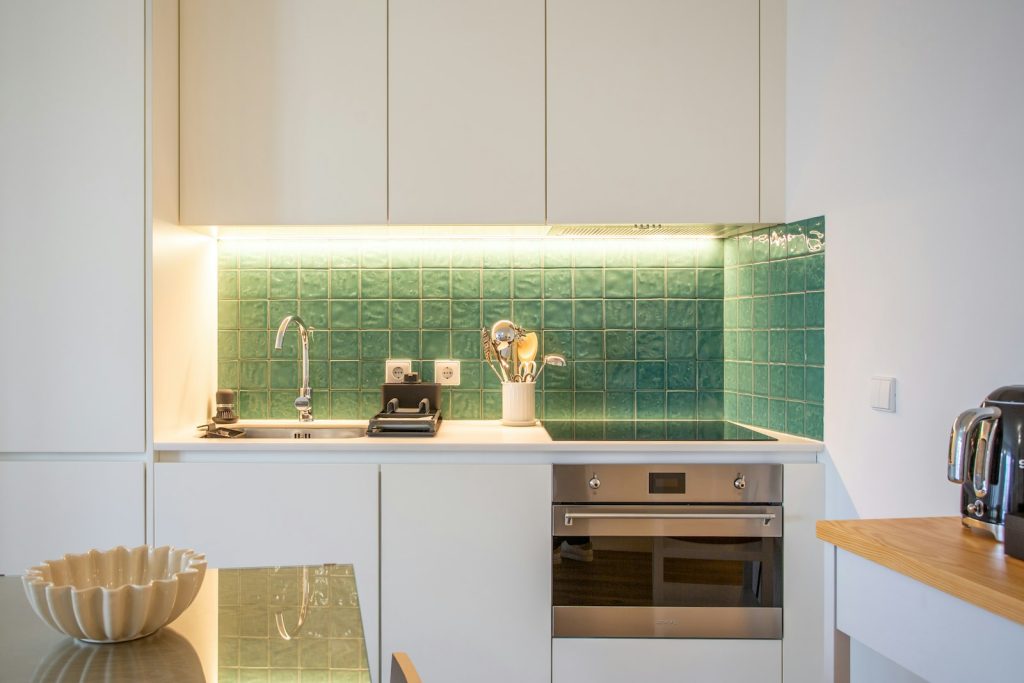 Compact kitchen with white units and a green tiled splashback