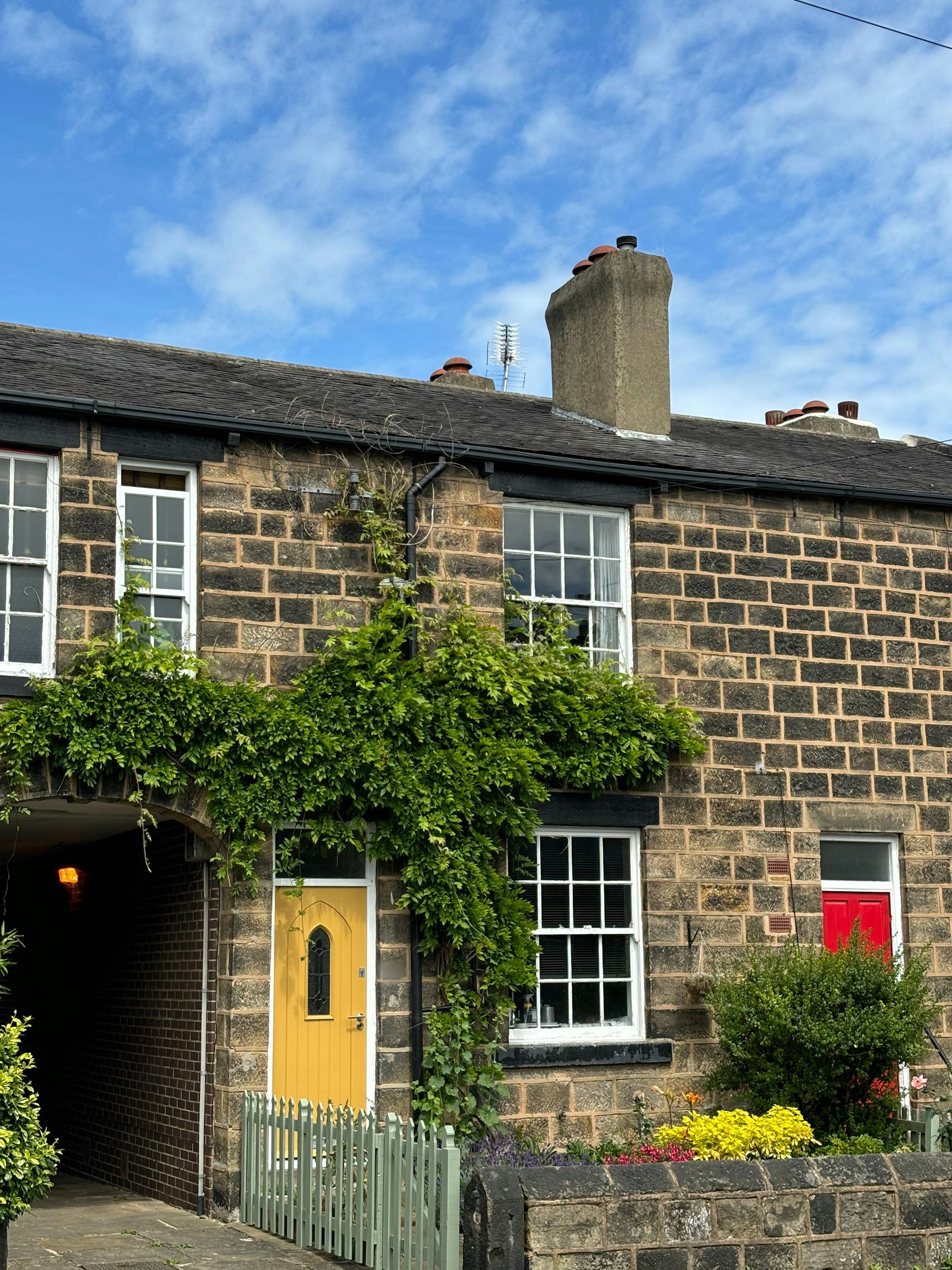 Victorian stone terraced cottage with a yellow front door and climbing ivy