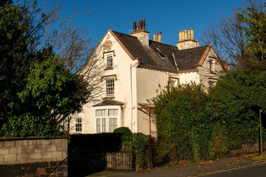 Cream-rendered Victorian detached house with gabled roof and tall chimneys behind a hedge