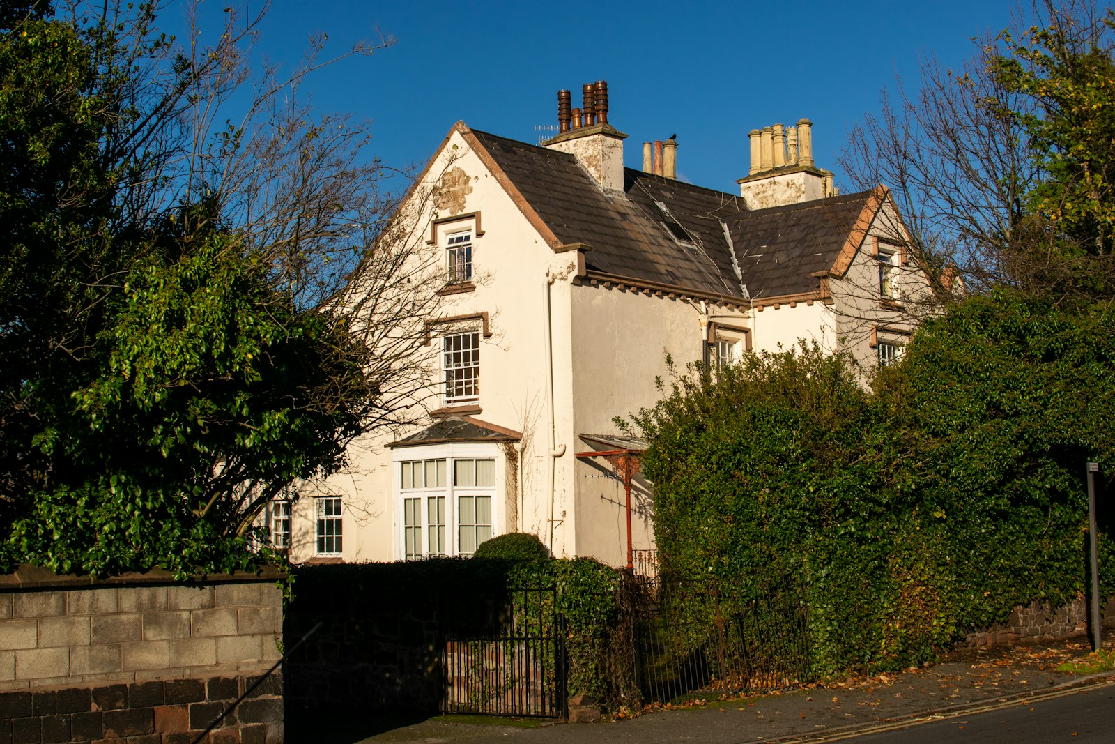 Cream-rendered Victorian detached house with gabled roof and tall chimneys behind a hedge