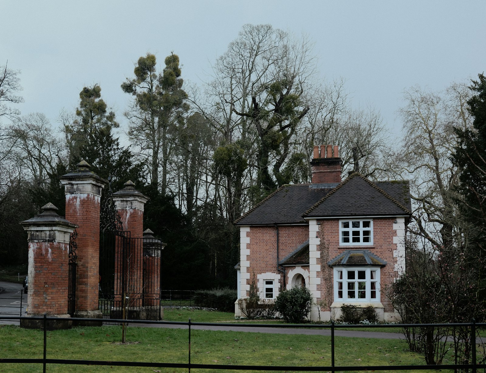 Red brick Victorian lodge house with white bay window beside brick gate piers