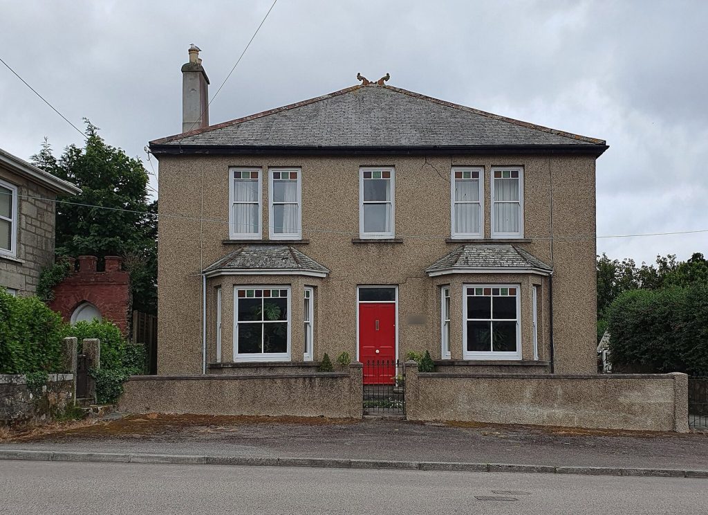 Edwardian rendered detached house with red front door and bay windows, Cornwall