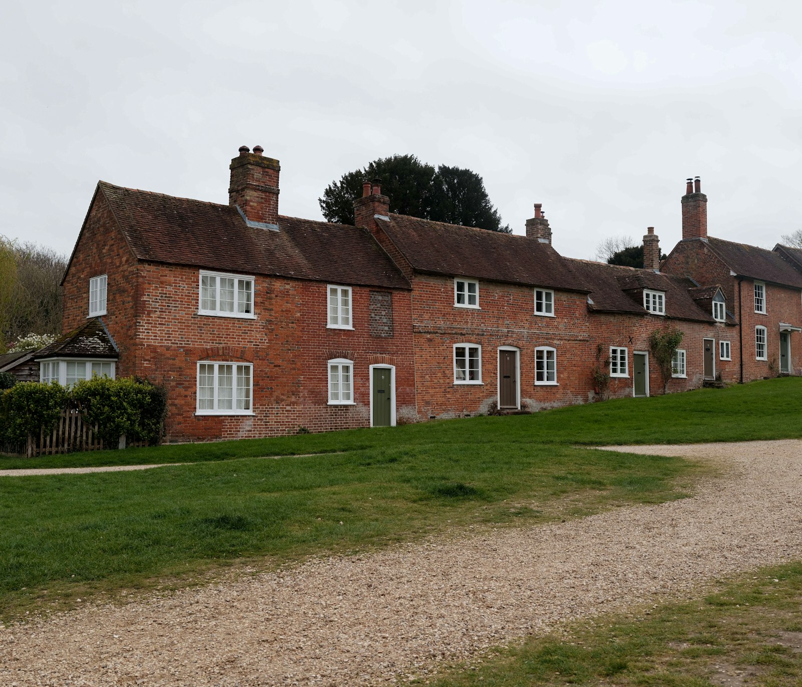Row of red brick cottages with white windows across a village green