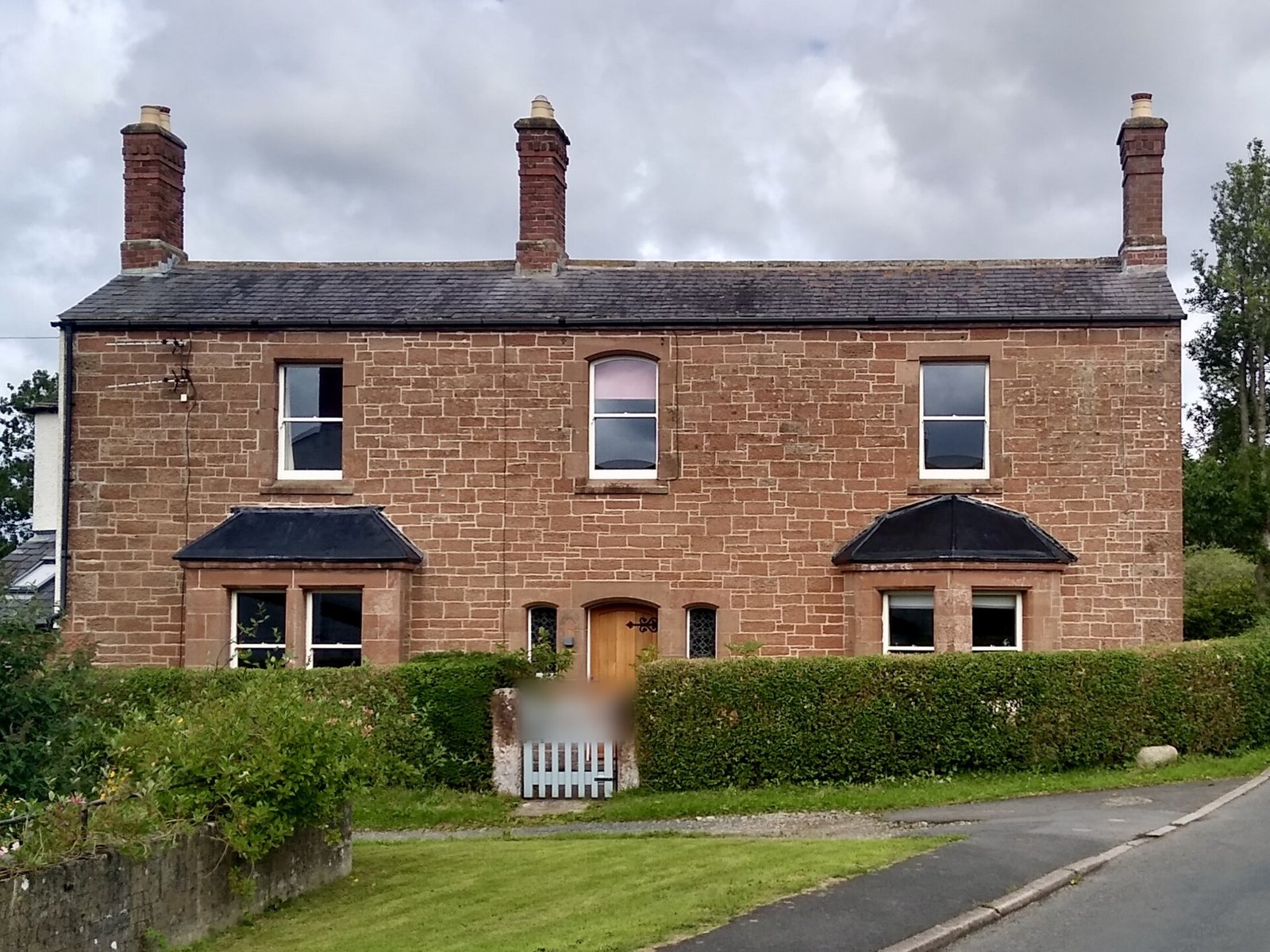 Red sandstone Victorian detached house with three chimneys, twin bays and an oak door behind a hedge