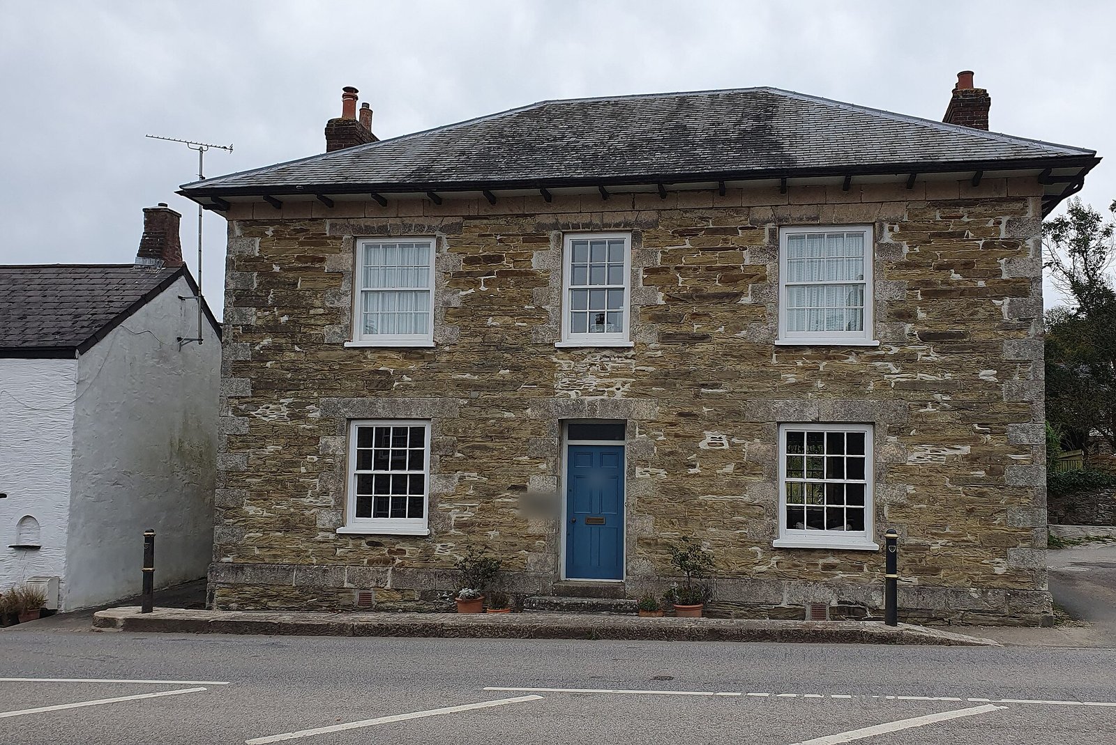 Symmetrical Georgian stone detached house with hipped slate roof, sash windows and a blue front door