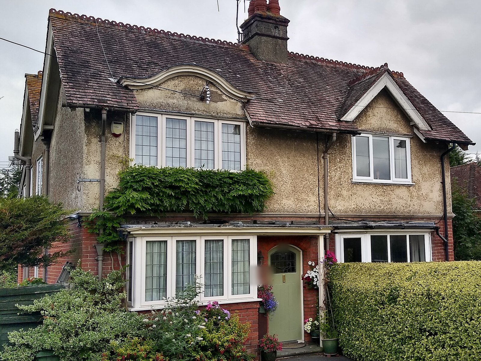 Edwardian semi-detached house with leaded bay windows, pebbledash first floor and red brick below, green front door behind a hedge, Pulborough, West Sussex