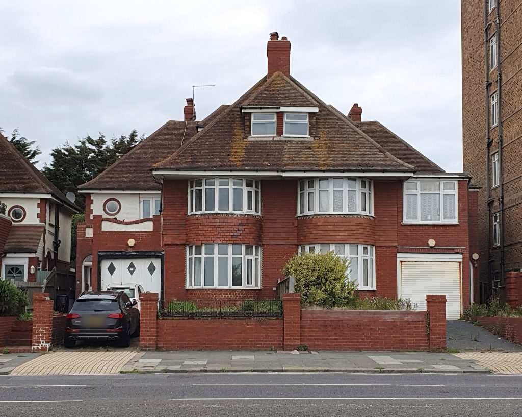 Red brick 1930s semi-detached pair with curved bay windows, dormer and integral garage behind a low brick wall, Hove, East Sussex