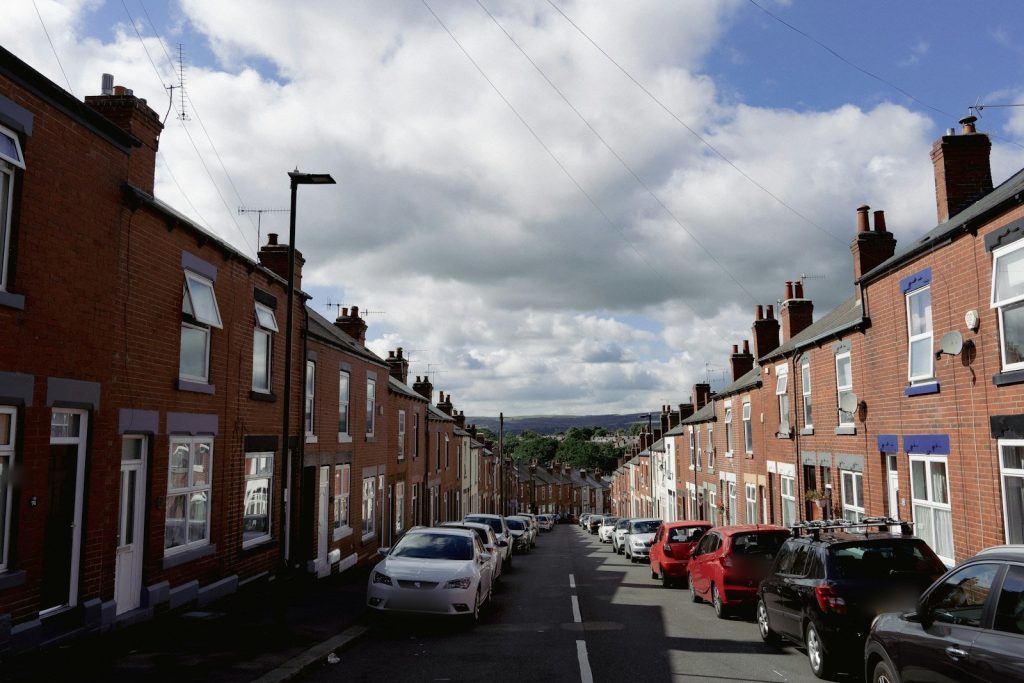 Red brick Victorian terraced street running downhill with parked cars